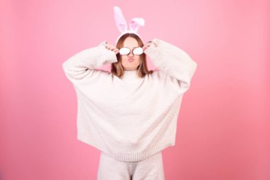 Tavşan kulaklı bir kız pembe arka planda dans ediyor. Paskalya tatili, gülümseme ve parti. Stüdyoda poz veren kadın. Paskalya yumurtalarıyla gözlerini kapatır, eğlenir..