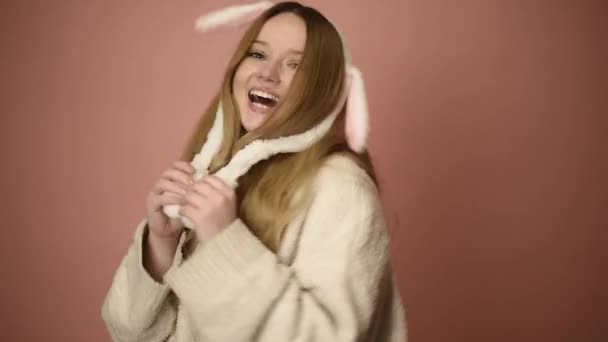 一个戴着粉红背景眼镜戴着兔子耳朵的漂亮女孩 复活节假期 长着小兔子耳朵的女人 摆出东方的架势 — 图库视频影像