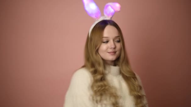 一个戴着粉红背景眼镜戴着兔子耳朵的漂亮女孩 复活节假期 长着小兔子耳朵的女人 摆出东方的架势 — 图库视频影像