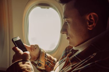 Yarısı boş bir uçakta telefonu olan bir adam. Akıllı telefona bakan bir gezgin.