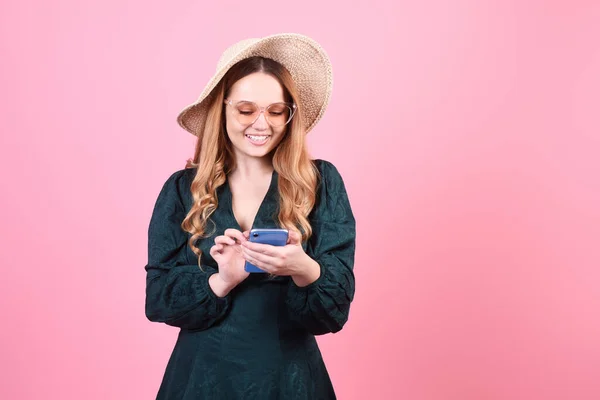 一个戴着草帽 戴着太阳镜 手里拿着手机 背景是粉色的女孩 短信和网络漫游 游客微笑 — 图库照片