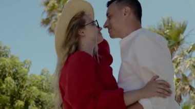 Modaya uygun bir çift palmiye ağaçlarının arkasında dans ediyor. Kırmızı elbiseli, gözlüklü, şapkalı, beyaz gömlekli bir adam. Tatil, tatil, yaz.