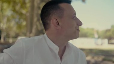 Parkın ve doğanın arka planında gülümseyen bir adam portresi. Beyaz gömlekli adam.