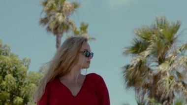 Happy girl in a red dress on vacation on the background of palm trees laughing and smiling. Vacation. A woman in sunglasses and a big hat enjoys life and dances.