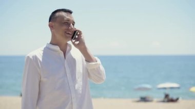 Sahilin, okyanusun ya da denizin arka planında beyaz gömlekli bir adam telefonla konuşuyor, telefon görüşmeleri yapıyor ve internette dolaşıyor. İş adamı tatilde, serbest çalışıyor..