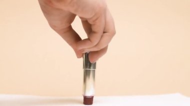 One lipstick crushed. A hand on a nude background crushes lipstick, it spreads