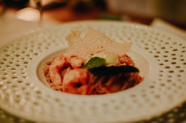 Yemek sırasında pahalı bir restoranda yemek fotoğrafı. Beyaz bir tabakta delikleri olan makarna ve karides.