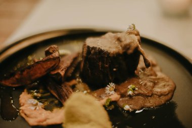 Yemek sırasında pahalı bir restoranda yemek fotoğrafı. Siyah tabakta et ve patates, yemek süslemede çiçekler.