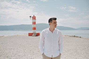 Beyaz gömlekli bir adam sahil boyunca yürür. Dağların arka planına karşı duran adam ve deniz kızıl fenere gider. Dinlen ve seyahat et.