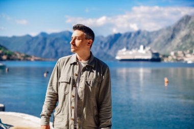 Bir adam denizin ve dağların arkasında gülümseyerek durur. Tatil ve açık hava eğlencesi. Tatildeki adam.