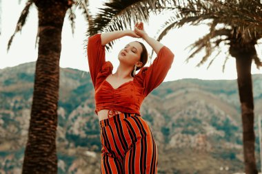 Yazın, palmiye ağaçları ve dağların arkasında şık bir kadın. Kırmızı elbiseli ve uzun küpeli İspanyol kız.