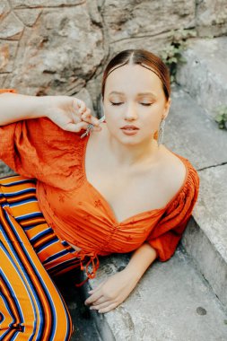 Merdivenlerde poz veren güzel bir esmer. Mücevher gümüş küpeler, profesyonel makyaj, sarı takım elbise. Zarif turist