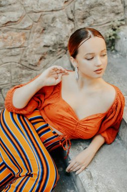 Merdivenlerde poz veren güzel bir esmer. Mücevher gümüş küpeler, profesyonel makyaj, sarı takım elbise. Zarif turist