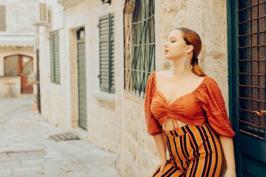 Eski şehirde kadın modası ve poz. Kapının yanında uzun küpeli ve turuncu takım elbiseli şık bir kız. Avrupa 'yı gezmek