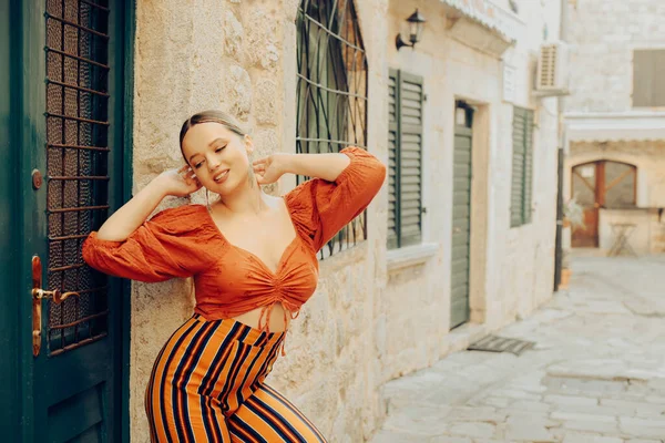 旧市街の女性のファッションとポージング ドアの近くに長いイヤリングとオレンジのスーツを持つ美しいスタイリッシュな女の子 ヨーロッパ中を旅する — ストック写真
