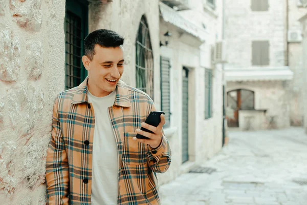 Portrait of a guy on the background of the old city with a phone. The guy writes a message and looks at the smartphone. Communication abroad, roaming, dating while traveling
