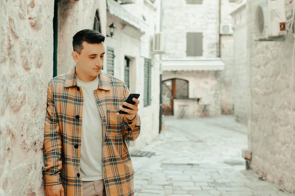 Portrait of a guy on the background of the old city with a phone. The guy writes a message and looks at the smartphone. Communication abroad, roaming, dating while traveling