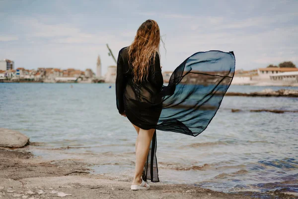 A woman with a flying pareo. Gorgeous brunette on the beach against the backdrop of the sea and the European city.