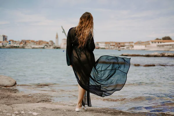 A woman with a flying pareo. Gorgeous brunette on the beach against the backdrop of the sea and the European city.