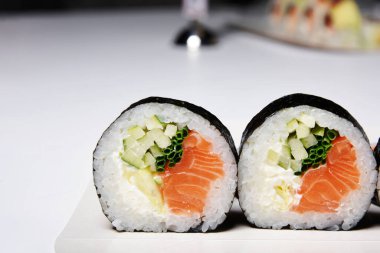 Sushi on a white background in sesame seeds with avocado and nigiri. Futomaki with salmon and cucumber. Food