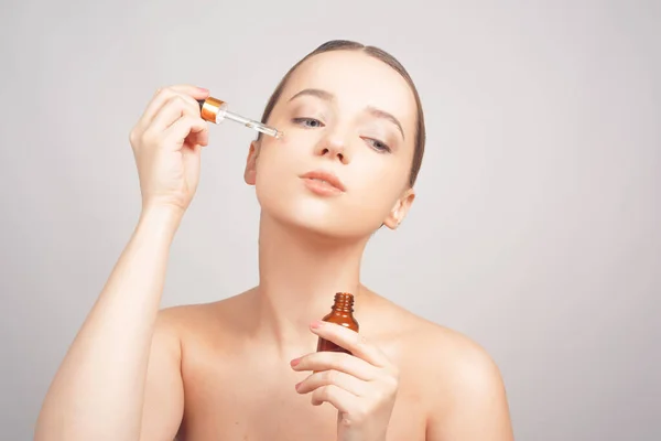 Girl on a white background skin care, oil, serum with a pipette on her face