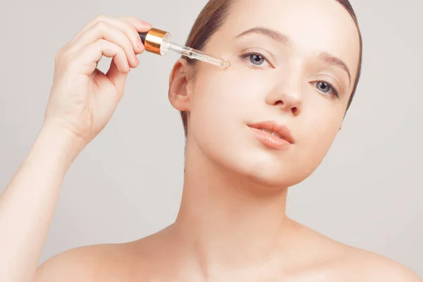 Girl on a white background skin care, oil, serum with a pipette on her face