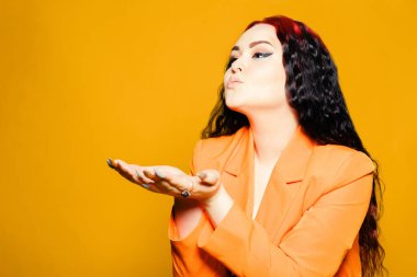 Turuncu arka planda tatlı bir kız. Kızıl saçlı, sarı elbiseli. Göz kalemi olan ve gülümseyen kız, eğlenceli kum öpücüğü veriyor.