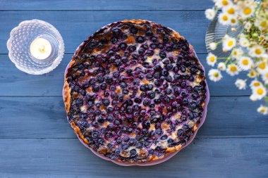 Mustikkapiirakka, bir Fin yabanmersinli turtası. Düz yatıyordu, üst görüntüsü mavi ahşap masa üzerinde beyaz çiçeklerle.