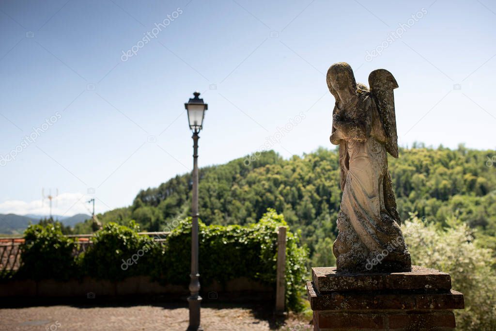 Statue of an angel outside Santa Maria and San Giorgio church in Fortunago, one of the most charming villages of Oltrepo Pavese, Lombardia countryside, Italy. Background with copy space.