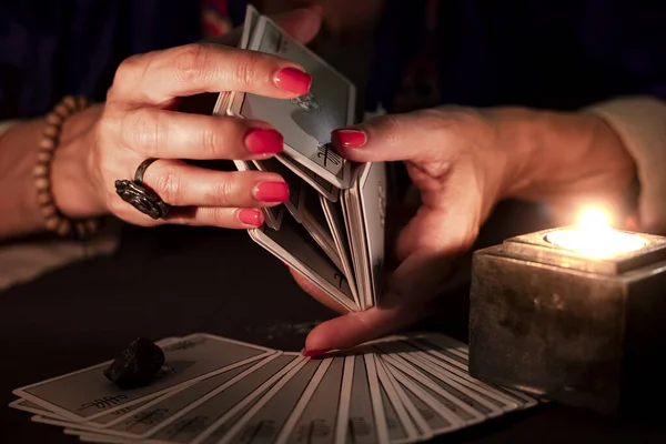 Fortune teller female hands shuffling a deck of tarot cards, during a reading. Close-up with candle light, moody atmosphere.
