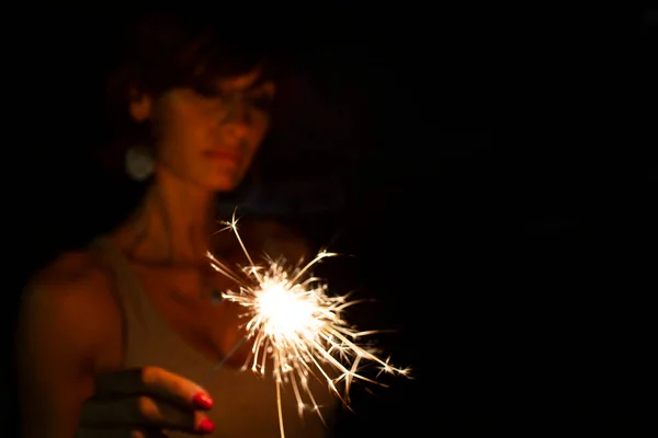 Attractive  caucasian woman, blurred face, holding a burning sparkler or bengal in the dark. Copy space. Holidays or magic background or wallpaper.