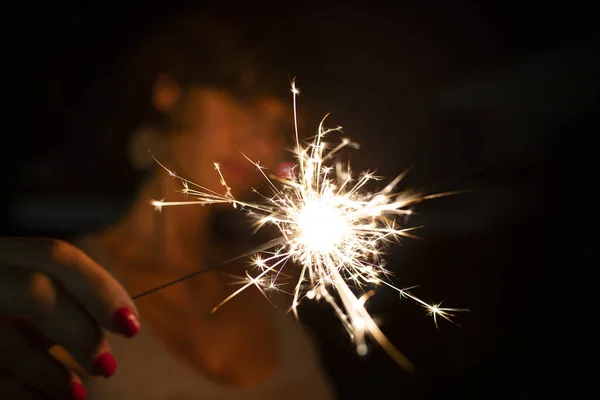 Attractive caucasian woman, blurred face, holding a burning sparkler or bengal in the dark. Copy space. Holidays or magic background or wallpaper.