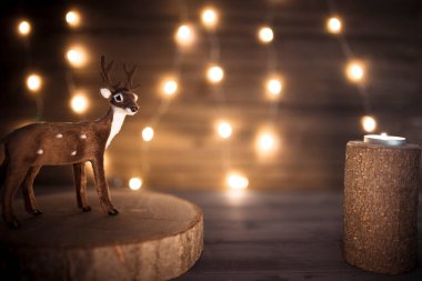 Minyatür ren geyiği ve ahşap mum. Arka planda parlayan ip ışıkları var. Kopya alanı olan Noel duvar kâğıdı.