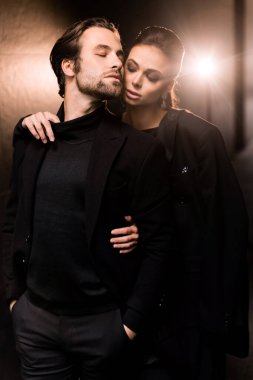 Siyah takım elbiseli ve ceketli genç çift stüdyoda poz veriyor.