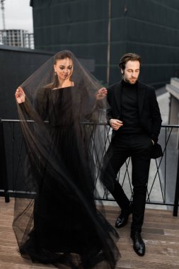 Siyah takım elbiseli, beyaz gömlekli genç çift duvarda poz veriyor.