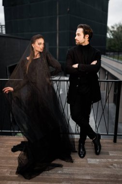 Siyah takım elbiseli genç bir çift ve arka planda siyah bir duvar var.