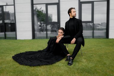 Parktaki bankta oturan siyah takım elbiseli ve beyaz gömlekli genç bir çift.