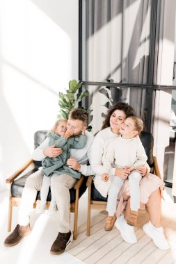 Genç ve mutlu bir aile evdeki sandalyelerde oturuyor. 