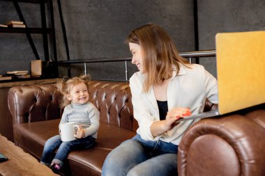 Genç anne ve kızı kanepede oturuyor ve dizüstü bilgisayar kullanıyorlar.