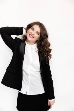 Siyah takım elbiseli güzel bir kadın beyaz arka planda poz veriyor.
