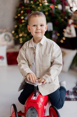 Küçük çocuk Noel ağacının yanında oyuncak arabasıyla oynuyor.