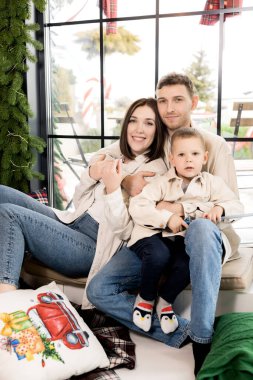 Evde süslü Noel ağacının yanında oturan sevimli aile, yeni yıl kutlaması konsepti. 