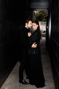 Siyahlar içinde dergi kapağı için fotoğraf çeken beyaz bir çift. Çekici sakallı genç kadın kameraya poz veriyor, manken konsepti.. 