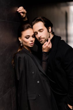 Siyahlar içinde dergi kapağı için fotoğraf çeken beyaz bir çift. Çekici sakallı genç kadın kameraya poz veriyor, manken konsepti.. 