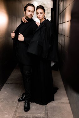 Siyahlar içinde dergi kapağı için fotoğraf çeken beyaz bir çift. Çekici sakallı genç kadın kameraya poz veriyor, manken konsepti.. 