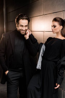 Siyahlar içinde dergi kapağı için fotoğraf çeken beyaz bir çift. Çekici sakallı genç kadın kameraya poz veriyor, manken konsepti.. 