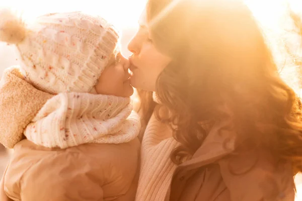 outdoors portrait of mother kissing her little daughter on the nose