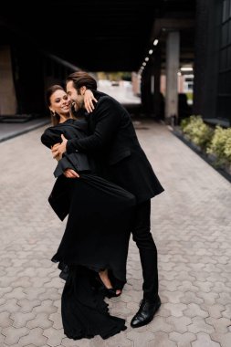 Mutlu evli çift sokaklarda dans ediyor, sarılıyorlar, şık siyah kıyafetler giyiyorlar. Yakışıklı sakallı adam muhteşem genç bayana sarılıyor, gülümsüyor, modern düğün kavramı.