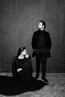 Siyahlar içinde dergi kapağı için fotoğraf çeken beyaz, şık giyinmiş beyaz bir çift resmi. Çekici sakallı genç kadın kameraya poz veriyor, manken konsepti.. 