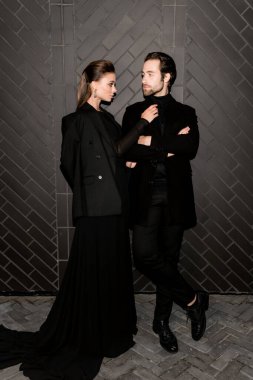 Siyahlar içinde dergi kapağı için fotoğraf çeken beyaz bir çift. Çekici sakallı genç kadın kameraya poz veriyor, manken konsepti.. 